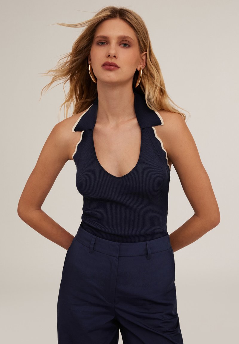 Marinblå ribbad linne med djup V-ringning och kontrasterande krämfärgad kant vid kragen. Matchas med marinblå högmidjade byxor.