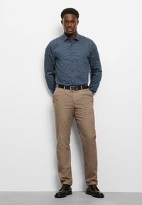 Marineblaues Hemd mit geometrischem Muster, braune strukturierte Hose und dunkle Schuhe. Das Hemd verfügt über einen Kragen und eine Knopfleiste.