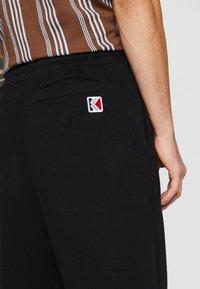 Sorte sweatpants med en glat tekstur har en baglomme og et lille, broderet logo i rød, hvid og blå.