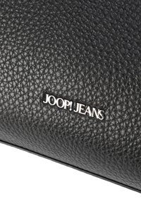 Schwarze, strukturierte Lederoberfläche mit aufgenieteten Buchstaben des silbernen Metalls "JOOP! JEANS".