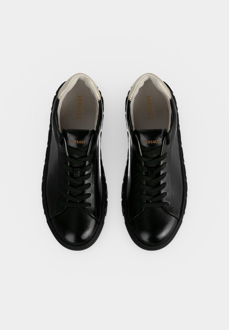 Paar schwarze Leder-Versace-Sneaker mit schwarzen Schnürsenkeln und weißem Innenfutter, nebeneinander auf weißem Hintergrund dargestellt.