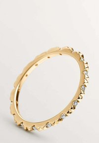 Anillo de oro con un borde acanalado, engastado con pequeñas piedras preciosas redondas y transparentes, mostrado sobre un fondo claro y sencillo.