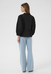 Zwarte blouse met opgeblazen mouwen en een hoge hals, met geplooide details, gecombineerd met lichtblauwe wijde denim jeans.