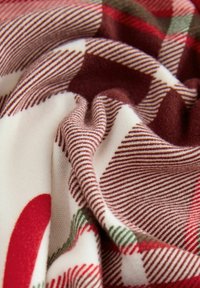 Knitted fabric featuring a multicolored plaid pattern with red, green, and cream hues; soft texture with visible stripes and smooth folds.