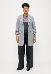 Grijze blazer met een getailleerd ontwerp en revers, gedragen over een gestreepte top en gecombineerd met brede zwarte broeken. Glad, gestructureerd stoffen.