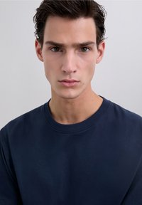 Marineblauw crewneck T-shirt gemaakt van zachte stof met een gladde textuur, voorzien van korte mouwen en een klassieke pasvorm, zonder zichtbare patronen of versieringen.