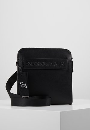 Černá crossbody kabelka Emporio Armani s vyraženým logem, zapínáním na zip a nastavitelným popruhem s visačkou projektu udržitelnosti.