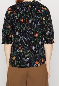 Sort bluse med blomsterprint i forskellige farver. Har puffede ærmer og en samlet halsudskæring. Lavet af letvægtsstof.