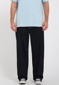 Vaqueros de mezclilla azul oscuro con corte relajado, combinados con una camiseta azul clara y zapatillas negras. Diseño simple, sin patrones ni acentos visibles.