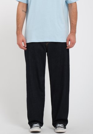 Dark blue denim jeans with a relaxed fit, paired with a light blue t-shirt and black sneakers. Simple design, no visible patterns or accents.