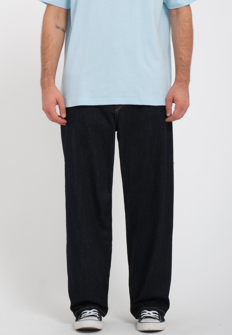 Vaqueros de mezclilla azul oscuro con corte relajado, combinados con una camiseta azul clara y zapatillas negras. Diseño simple, sin patrones ni acentos visibles.