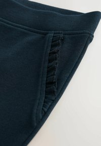 Dunkelgrüner Stoff mit glatter Textur, der an der Naht mit gerafften Details versehen ist. Die Kanten sind sauber genäht für Langlebigkeit.