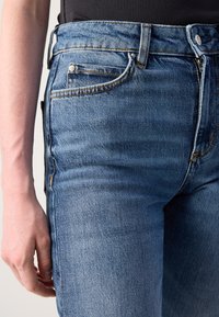 Blå denimjeans med rett kutt, med en lys vask, synlig stiching og en liten frontlomme. Jeansen har en jevn tekstur og et klassisk design.