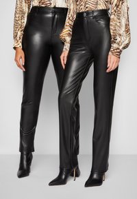 Zwarte faux leren broek met een fitted ontwerp, hoge taille en een rits aan de voorkant. Beide broeken hebben effen zijkanten en subtiele naden.