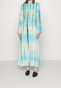 Dlouhé šaty s tílkovým vzorem v odstínech modré a zelené, se rovnou siluetou a dlouhými rukávy. Vydané s černými texturovanými nazouvacími botami.