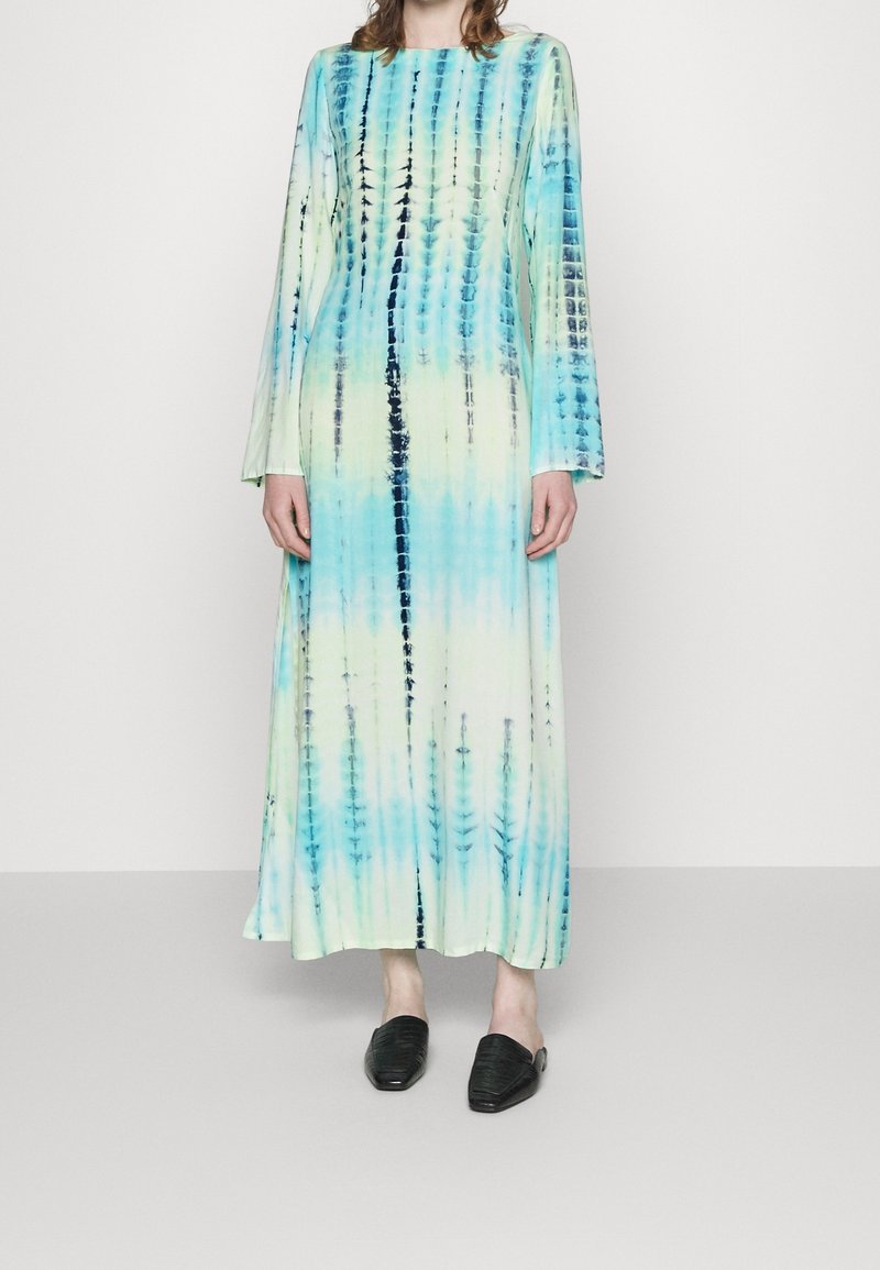 Dlouhé šaty s tílkovým vzorem v odstínech modré a zelené, se rovnou siluetou a dlouhými rukávy. Vydané s černými texturovanými nazouvacími botami.
