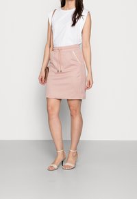 Falda rosa con estampado y cintura con cordón, combinada con una blusa blanca de manga corta y sandalias beige. Tejido suave con acentos sutiles.