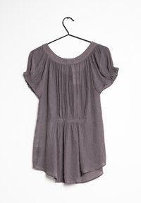 Blusa viola corta e ampia con dettagli arricciati su scollatura e vita, appesa a un gancio nero su sfondo bianco.