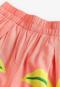 Shorts corail à taille élastique avec imprimés floraux jaunes et accents verts. Tissu texturé avec des plis pour un détail supplémentaire.