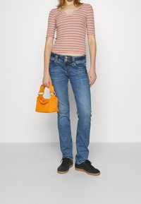 Randig röd och vit åtsmitande t-shirt, blå denimjeans, orange handväska med korta handtag och svarta sneakers med bruna sulor.
