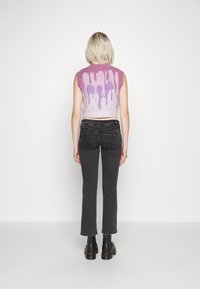 Avskuren ärmlös tröja i ljuslila med ett droppande mönster; parat med högmidjade svarta jeans och svarta ankelstövlar.