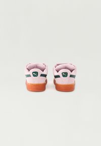 Baskets en daim rose avec des accents verts, caractéristiques d'une semelle en caoutchouc et d'un talon marqué. Texture lisse et design classique à tige basse.