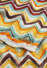 Flerfarvet strikket stof med zigzagmønster i gult, turkis, brunt og orange med en metalisk "Superdry"-mærkat.