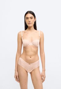 Világos rózsaszín fehérnemű szett, mely mintás csipkés melltartóból alátámasztó drótlemezzel és hozzá illő, félig átlátszó, hullámos szélű bugyiból áll.