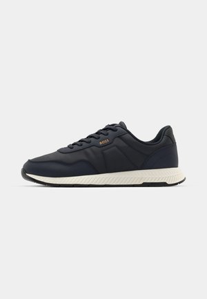 Zapatilla deportiva azul marino con parte superior sintética lisa, acentos texturizados, suela ligera y suela de goma neutra con un patrón en zigzag.