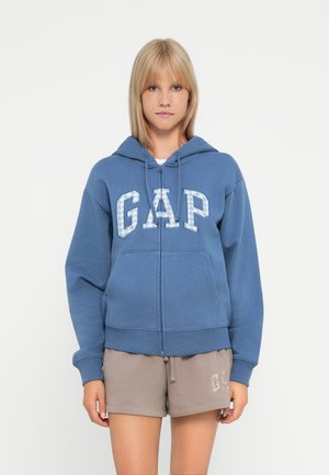 Blue zip-up hoodie with a large, light blue "GAP" logo on the front. Features a drawstring hood and front pockets. Soft cotton material.