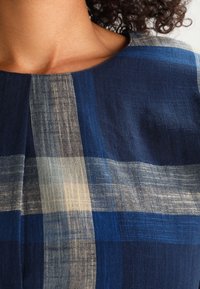Sininen ja beige ruudullinen kangas, jolla on sileä pinta; siinä on vaihtelevaa sinisen ja valkoisen sävyä vaakasuorissa ja pystysuorissa raidoissa.