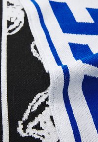 Knit scarf with blue, black, and white colors; features bold lettering and a repeating pattern of a stylized figure along the edges.