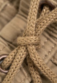 Primer plano de una cuerda trenzada beige atada en un nudo a través de un ojal metálico sobre una tela texturizada.