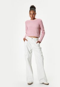 Pull court texturé rose et pantalons cargo blancs à jambes larges avec poches latérales, associés à des chaussures sans lacets beiges.