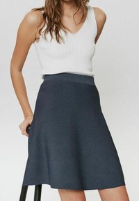 Tummanharmaa liehukehelmainen hame, valmistettu pehmeästä, joustavasta kankaasta; siinä on korkea vyötärönauha ja sileä pinta. Yhdistetty valkoiseen ribbineulottuun hihattomaan toppiin.