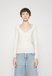 Maglia a maniche lunghe, attillata, in morbido tessuto color crema con scollo a barca e dettaglio a torsione sul petto. Maglia a trama con costine.