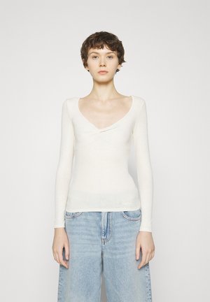 Maglia a maniche lunghe, attillata, in morbido tessuto color crema con scollo a barca e dettaglio a torsione sul petto. Maglia a trama con costine.