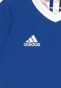 T-shirt de sport bleu en tissu lisse, avec un col blanc et un logo Adidas brodé en blanc sur le devant.