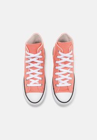 Zapatillas altas hechas de lona de color coral, con cordones blancos y suelas de goma negras. Punta redondeada con una tapeta blanca y detalles de costura.