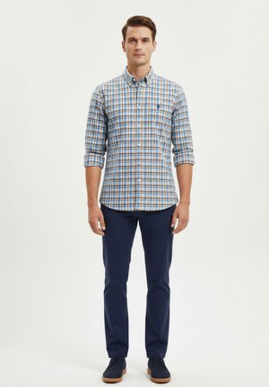 Camisa de cuadros en tonos de azul, naranja y blanco; mangas largas remangadas. Combinada con pantalones azul marino y zapatos oscuros.