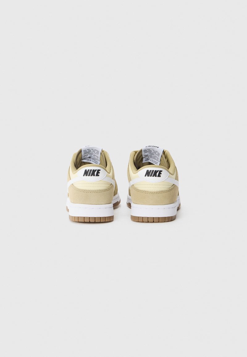 Baskets Nike avec une palette de couleurs jaune et crème, en matériau suédé, accents blancs et semelle en caoutchouc naturel, présentant un logo sur les talons.