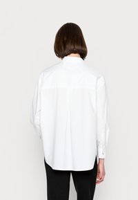 Fehér pamut ing laza szabással, hosszú ujjakkal, gombos mandzsettával és redőzettel a hátulján. Sima felület és klasszikus gallér kialakítás.