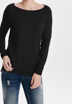 T-shirt noir à manches longues avec un décolleté large et une texture lisse, associé à un jean bleu déchiré avec des accents décolorés et des trous.