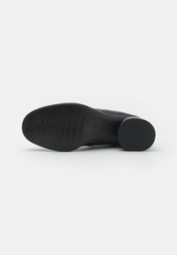Black shoe with a textured rubber sole, featuring horizontal ribbing and a rounded heel. Smooth upper surface with no visible accents.
