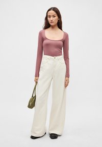 Tumevioletne, pika varrukaga pluus kaardus kaelusega, millele on kombineeritud laiad valged püksid ja väike roheline käekott. Mustad paksud saapad.