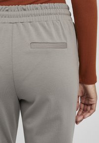 Lys grå joggesko med elastisk midje og baklomme. Stoffet ser glatt ut med en subtil tekstur.