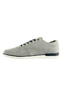 Zapatillas de lona grises con puntera redondeada, que presentan cordones oscuros en contraste, una suela blanca de perfil bajo y sutiles detalles de costura en los laterales.