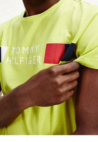 Camiseta de algodón verde lima con el texto "TOMMY HILFIGER". Presenta acentos en bloque en rojo, azul marino y blanco en el pecho y la manga.
