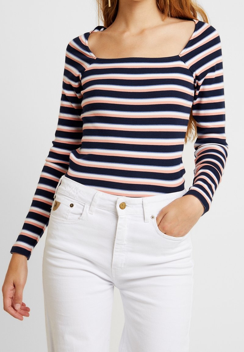 Langärmliges Oberteil mit quadratischem Ausschnitt in Marineblau, Rosa und Hellblau mit horizontalen Streifen, kombiniert mit hochgeschnittenen weißen Jeans. Weicher gerippter Stoff.
