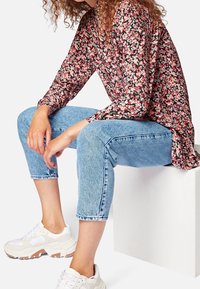 Top floreale a maniche lunghe con fiori rossi e rosa su uno sfondo nero, abbinato a jeans cropped blu chiaro e sneakers bianche.